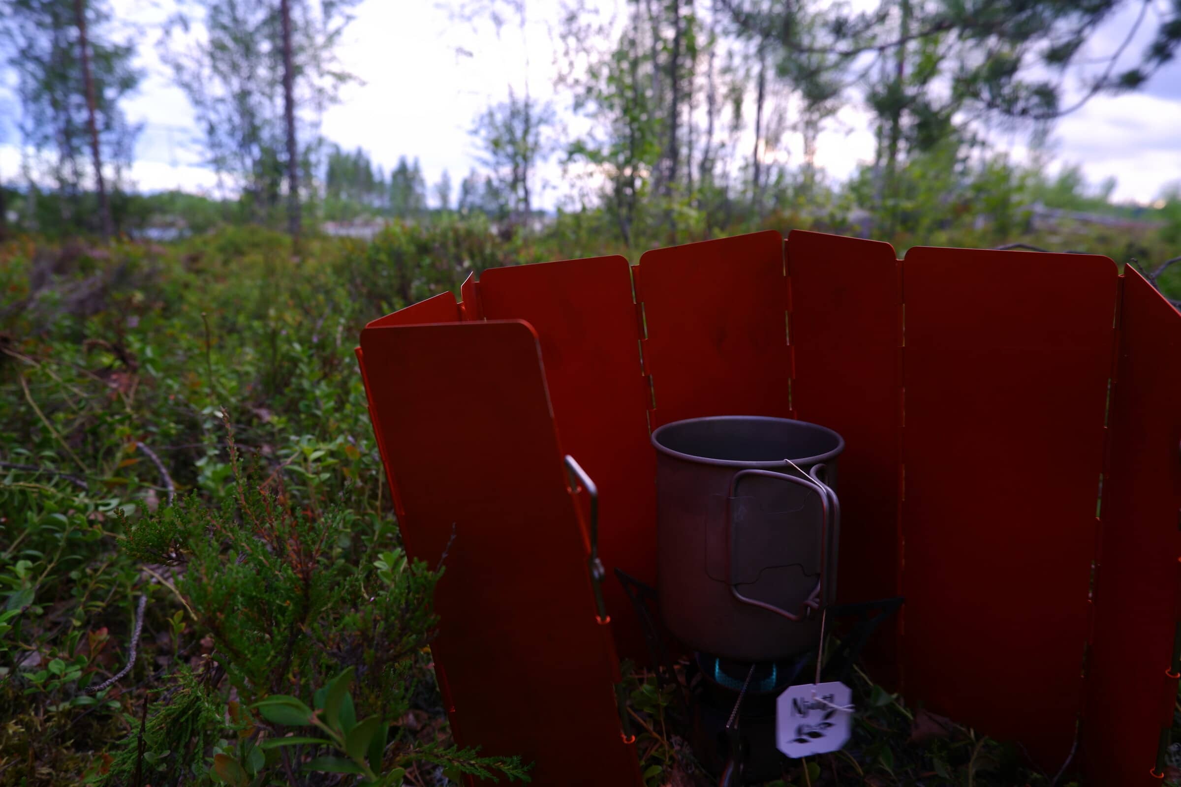 A camping mug on a multifuel burner with a teabag in it. There's a bit of steam rising as its coming up to a boil.