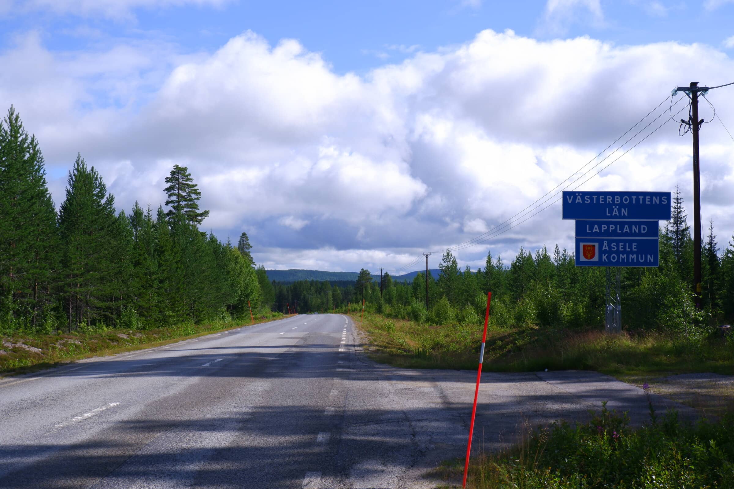 Asphalt road with a blue sign on the right side saying Västerbottens Län, Lappland, Åsele Kommun.