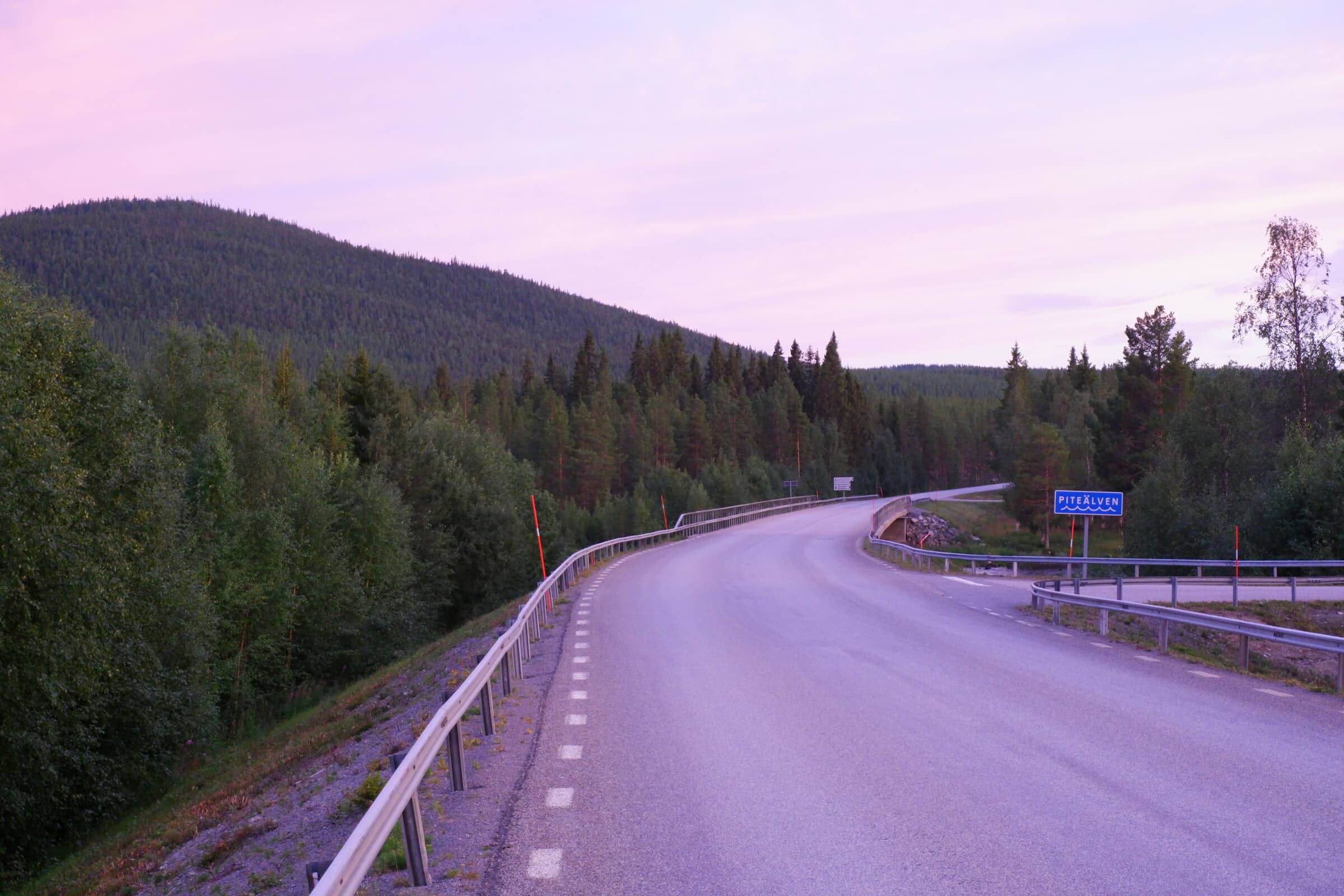 The road down to Piteälven. Sky is purple, with forest on the sides of the road.
